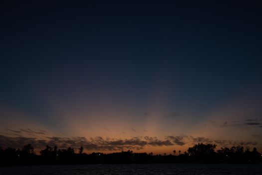 A peaceful sunset with silhouetted trees and calm water, creating a serene twilight scene.