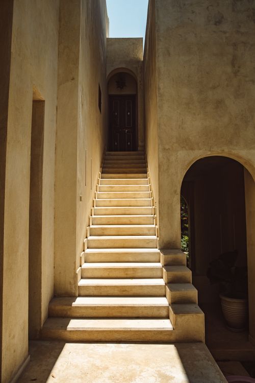 Free Sunlit staircase between concrete walls leading to a wooden door in a narrow courtyard. Stock Photo