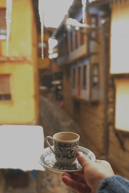 Hand holding a decorative coffee cup overlooking rustic street view.