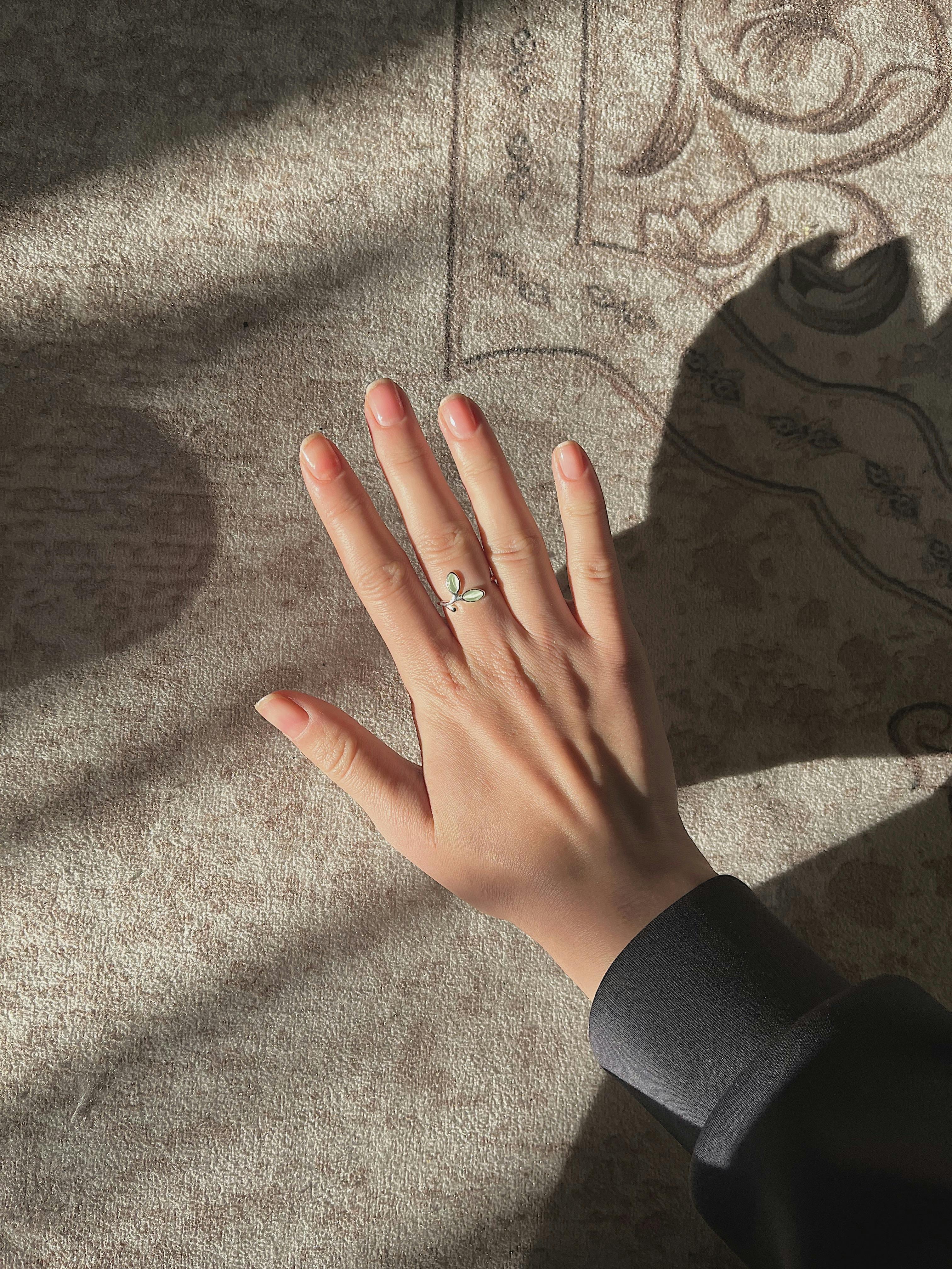 Close-up of a hand with a delicate silver ring on a sunlit textured surface.
