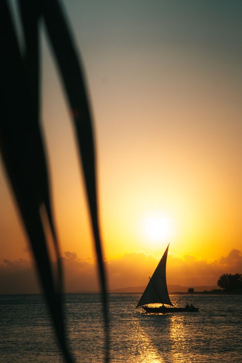 Free A peaceful sailboat silhouette against a vivid sunset over the ocean, creating a serene maritime scene. Stock Photo