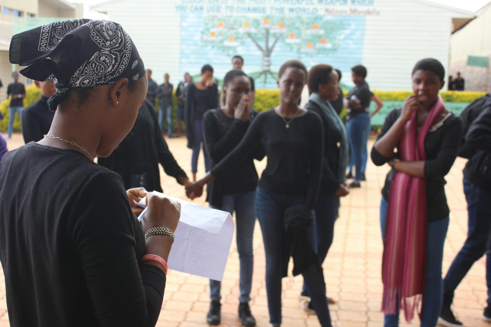 Women gathered outdoors in Burundi, engaging in community activities and reading a paper.