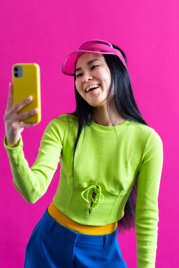 Teenage Girl Dressed In Colourful Outfit Looking At Yellow Mobile With Smile