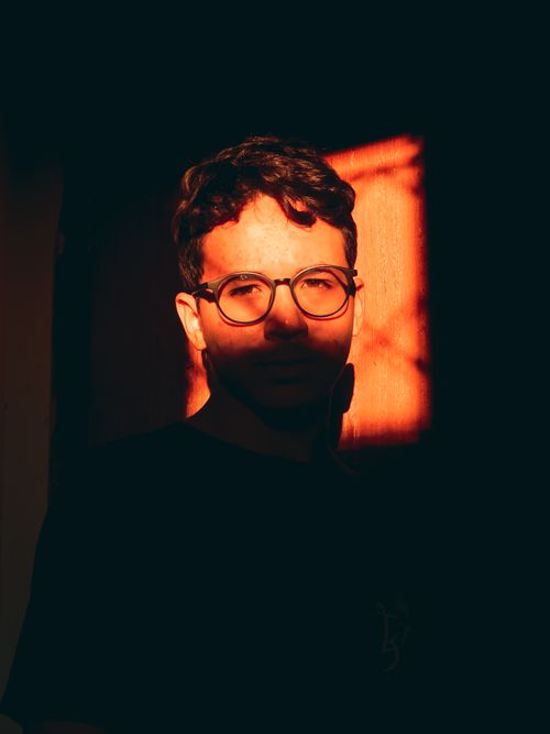 Free Moody portrait of a man with eyeglasses illuminated by dramatic warm light casting shadows over his face. Stock Photo
