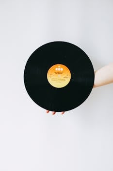 A hand holding a vintage vinyl record against a clean white backdrop.