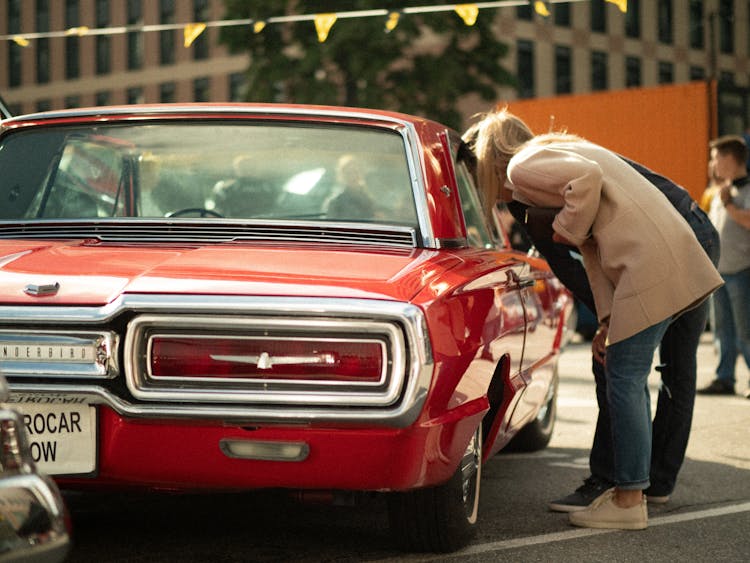 A Man And Woman Looking The Red Car 