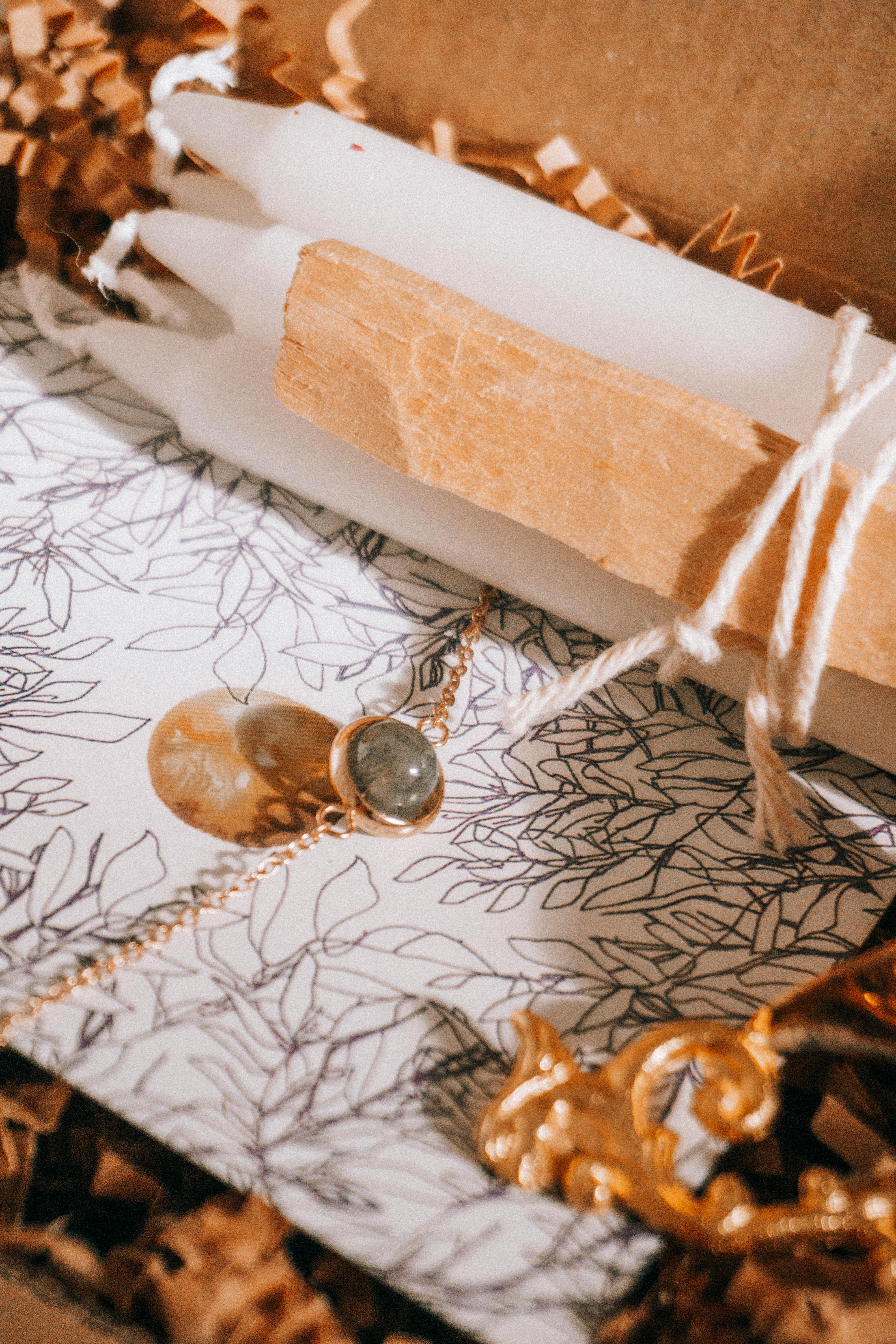 Aesthetic arrangement of candles, necklace, and ornate accessories on a floral patterned background.