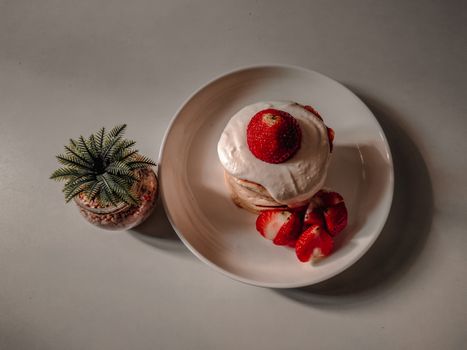 Flat lay of fluffy pancakes topped with strawberries and cream, perfect for breakfast.