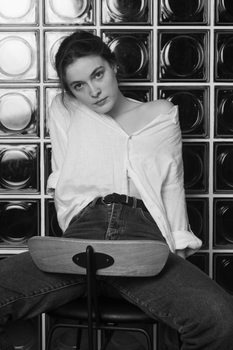 Grayscale portrait of a young woman sitting on a chair with a casual, stylish demeanor.