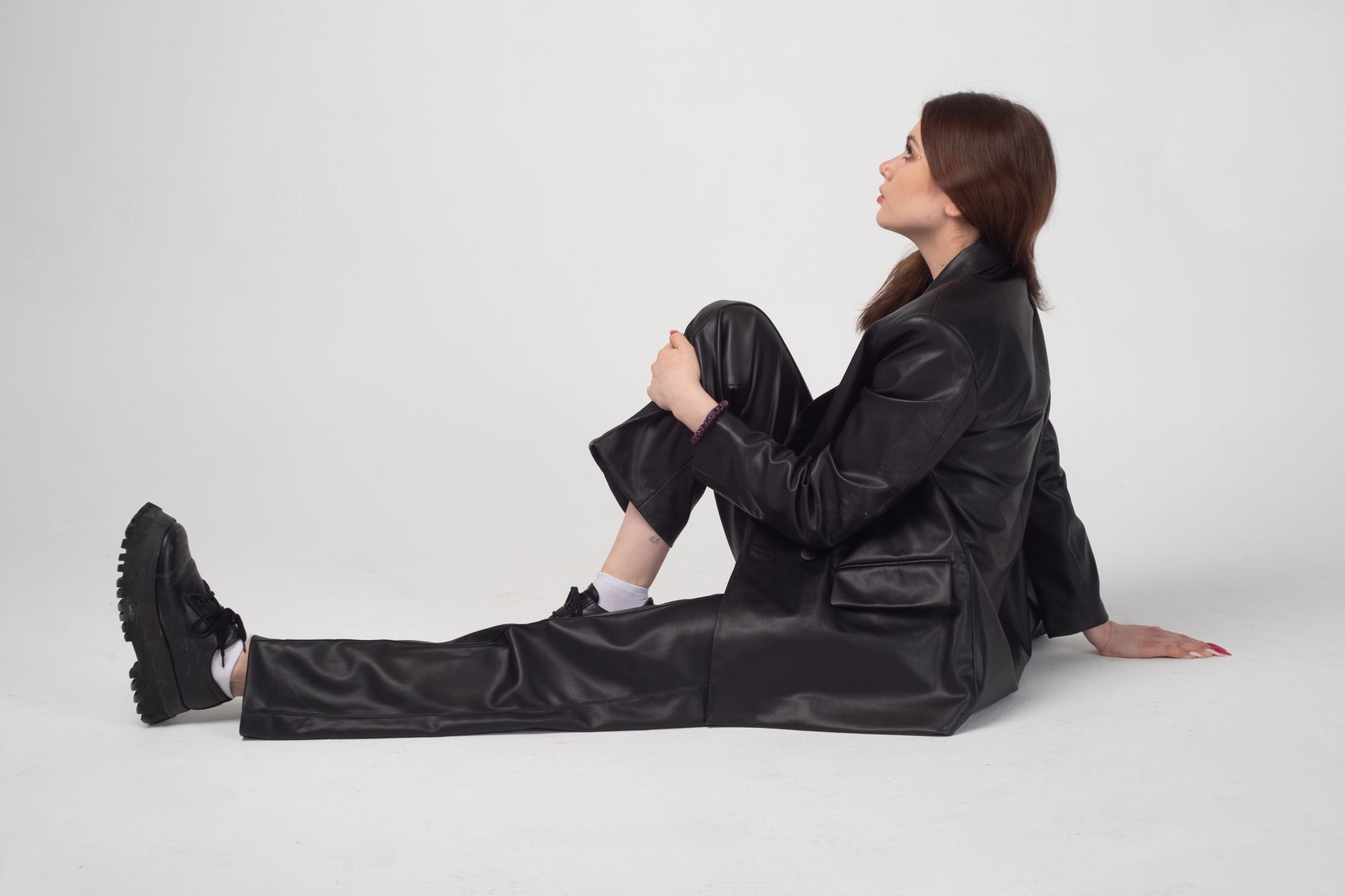 Studio portrait of a woman sitting on the floor in black leather attire, looking upwards.