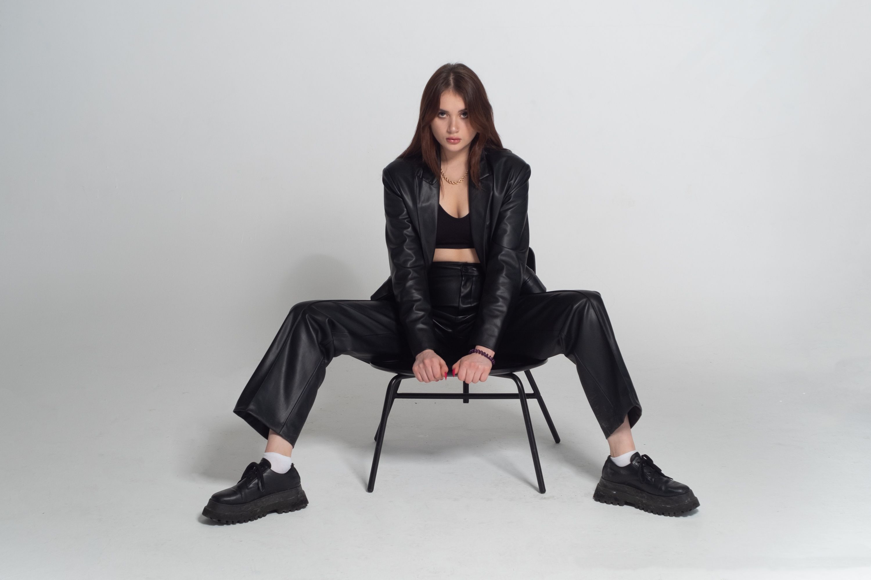 Stylish young woman in black leather jacket posing confidently in a studio setting.