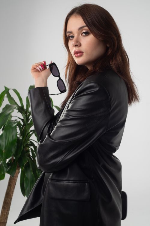 Free A fashionable woman wearing a leather jacket poses indoors, holding sunglasses and exuding confidence. Stock Photo