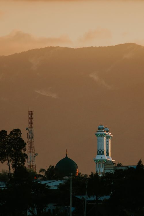 Free Stunning view of an Islamic minaret and mosque dome with mountains in the sunset background. Stock Photo