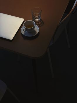 Elegant coffee cup and laptop on a cozy wooden table in low light.