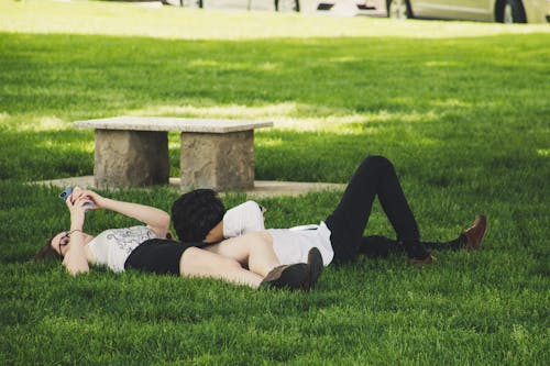 Free Man And Woman Laying On Green Grass Near Concrete Bench Stock Photo