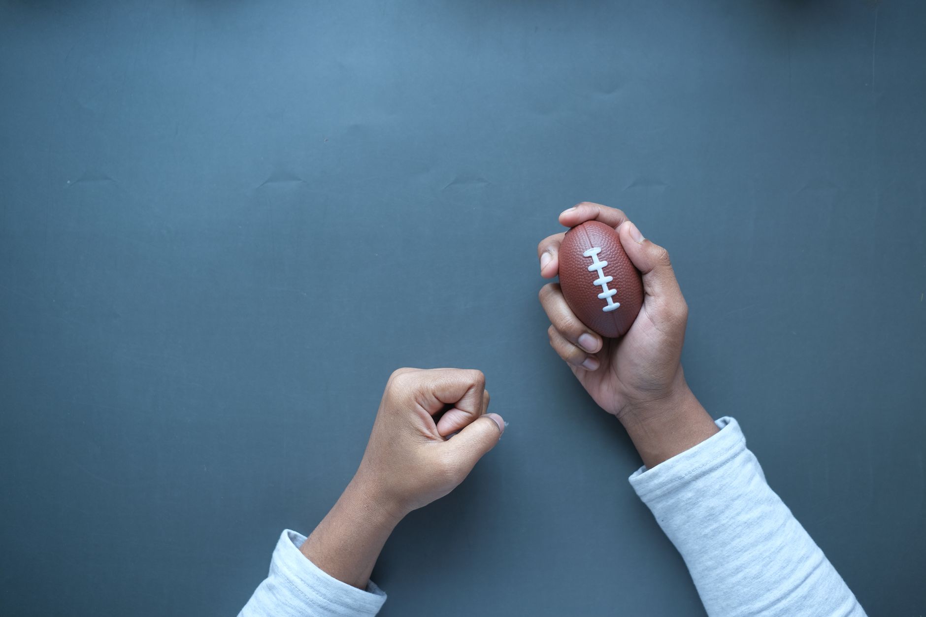 Hands holding a mini football on a blue surface, perfect for sports-themed designs.