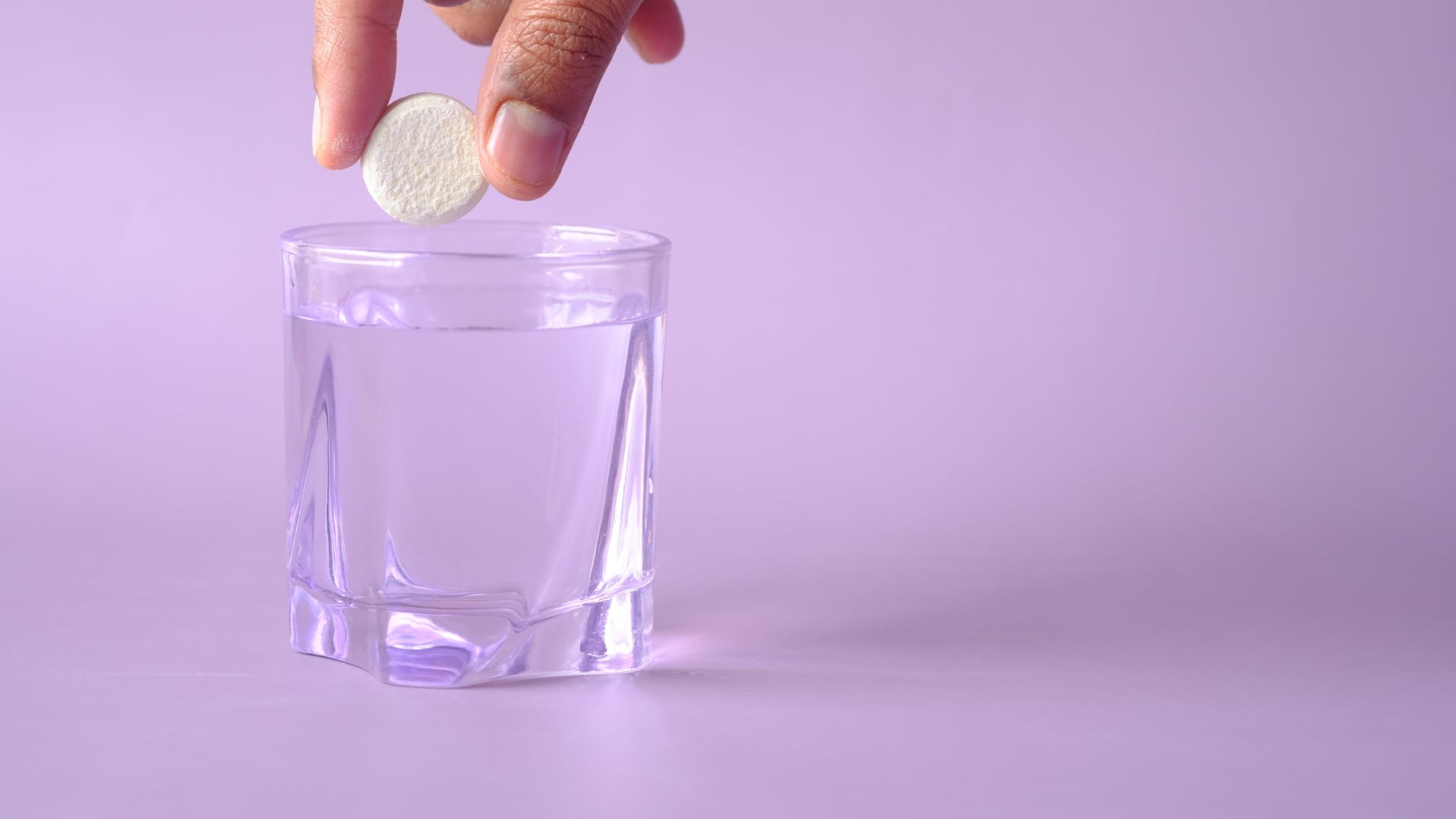 Unleashing Modafinil's Benefits: A Comprehensive Guide Close-up of a tablet being dropped into a glass of water on a purple background, creating bubbles.