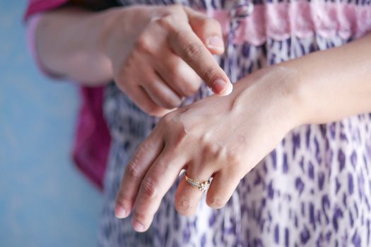 A woman applies skincare cream on her hand, highlighting moisturizing routine.