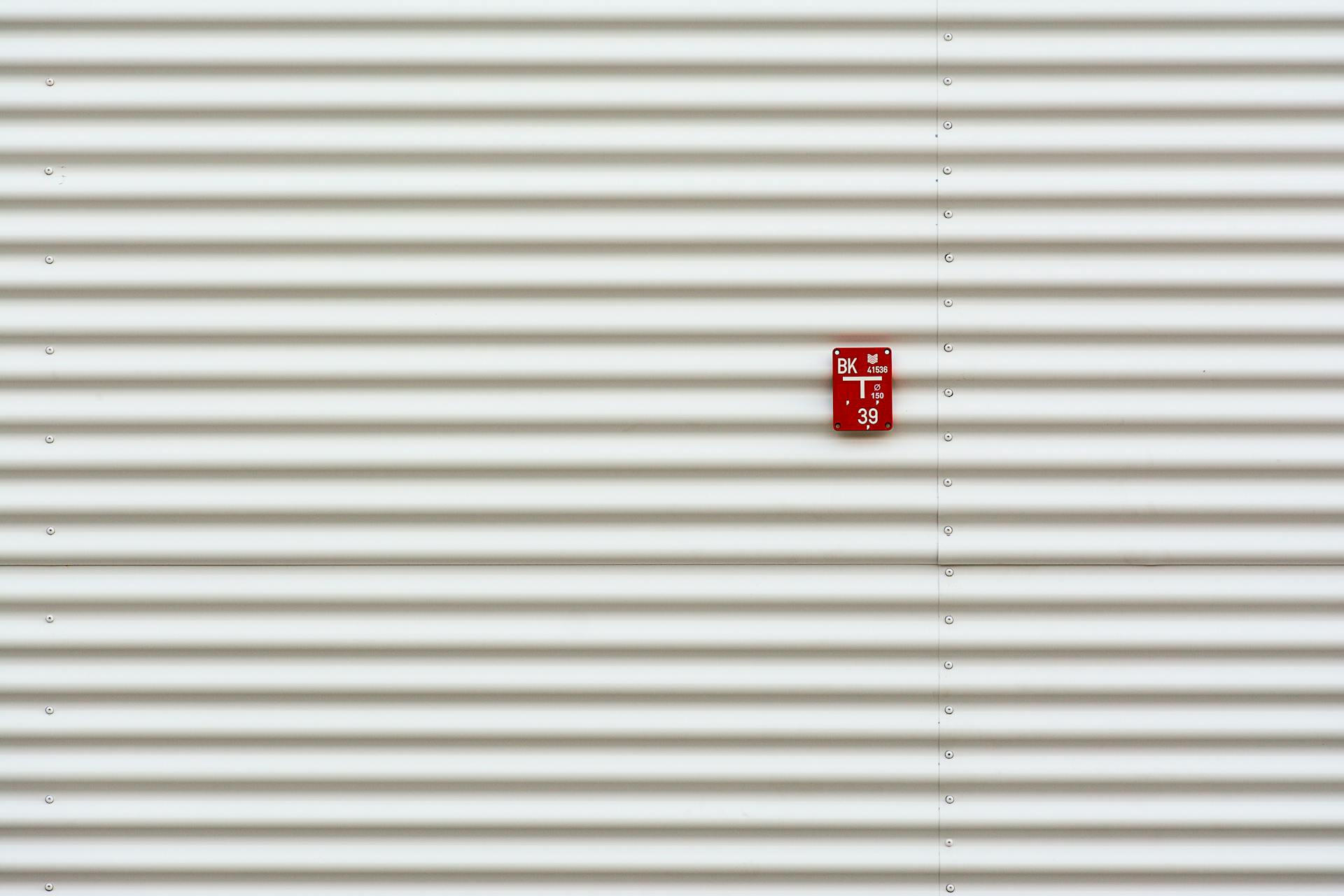 Minimalist image of corrugated metal wall with a red sign offering ample copy space.