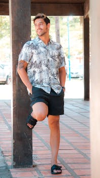 Man in floral shirt and shorts posing outdoors with a smile, showcasing casual fashion.