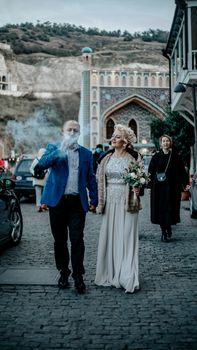 Elegant couple walking on cobblestone street with wedding bouquet. Unique backdrop.