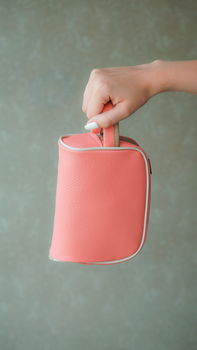 A close-up of a hand holding a pink cosmetic bag with a neutral textured background.