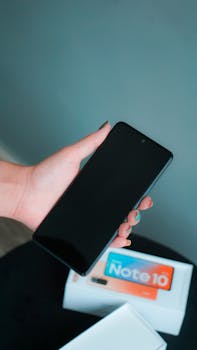 Close-up of a hand holding a smartphone above a new gadget box, suggesting a modern tech setup.