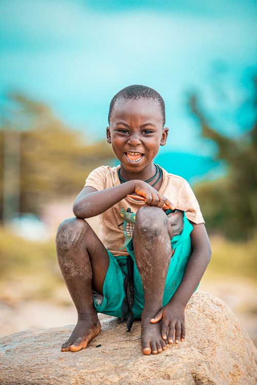 Free A happy young boy sitting barefoot on a rock enjoying a sunny day outdoors. Stock Photo