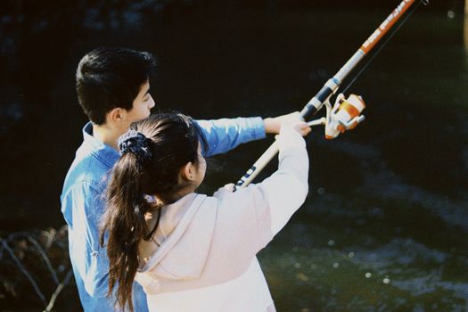 Young couple enjoying fishing at a tranquil lake, sharing a fishing rod.