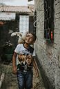 Smiling Boy with White Chicken on His Shoulder Walking in Backyard along House Wall