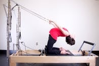 一名女子在灯光明亮的健身房中，使用普拉提改良器进行伸展运动