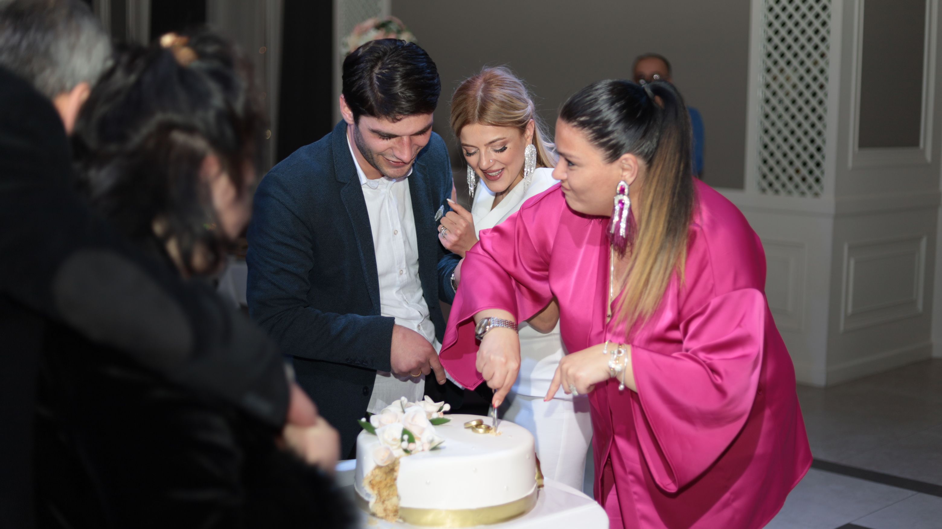 Joyful indoor celebration with people cutting a cake together.