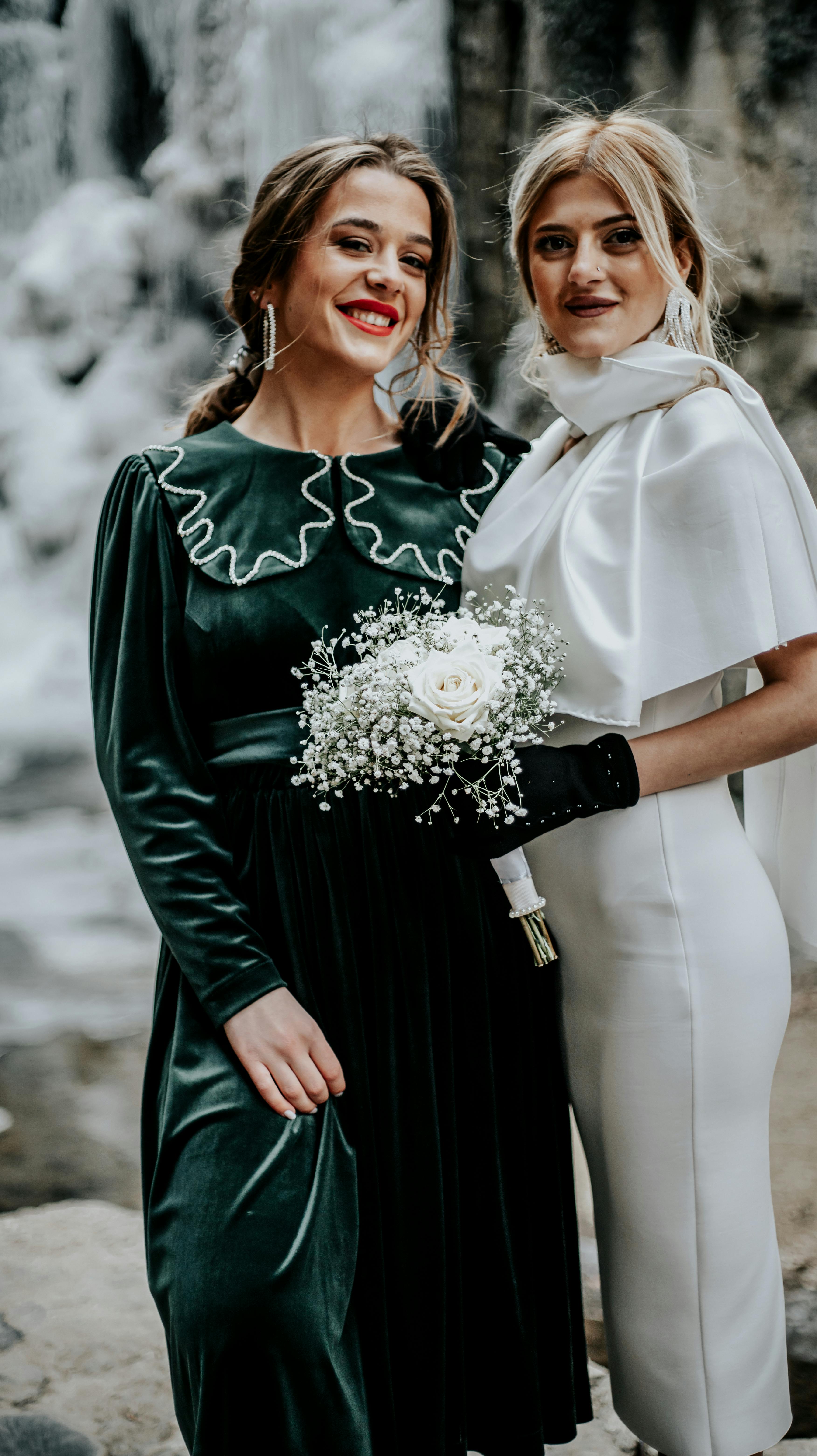 Two elegant women posing joyfully with a bouquet at a wedding setting.