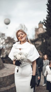 Bride in a white dress with black gloves holding a bouquet outdoors in winter.