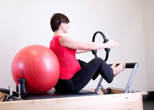 Free Woman in Red Top Leaning on Red Stability Ball Stock Photo