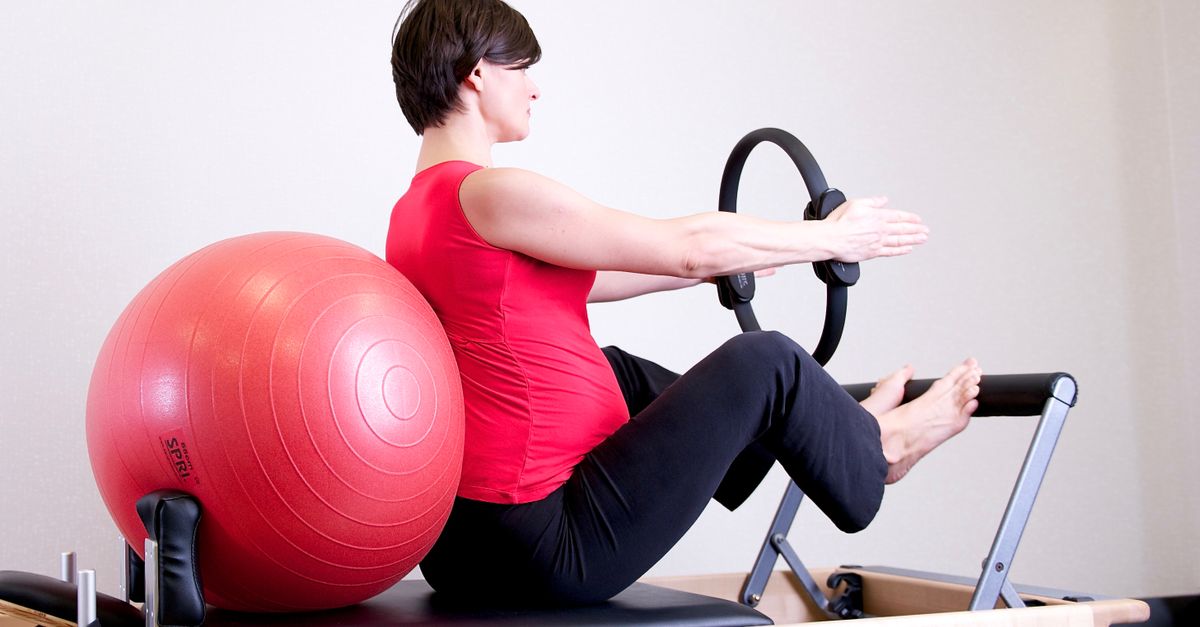 Pregnant woman in gym doing Pilates exercise with reformer and stability ball.