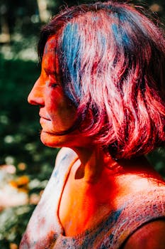 An adult woman with colorful powder on her face celebrating the vibrant Holi festival outdoors.