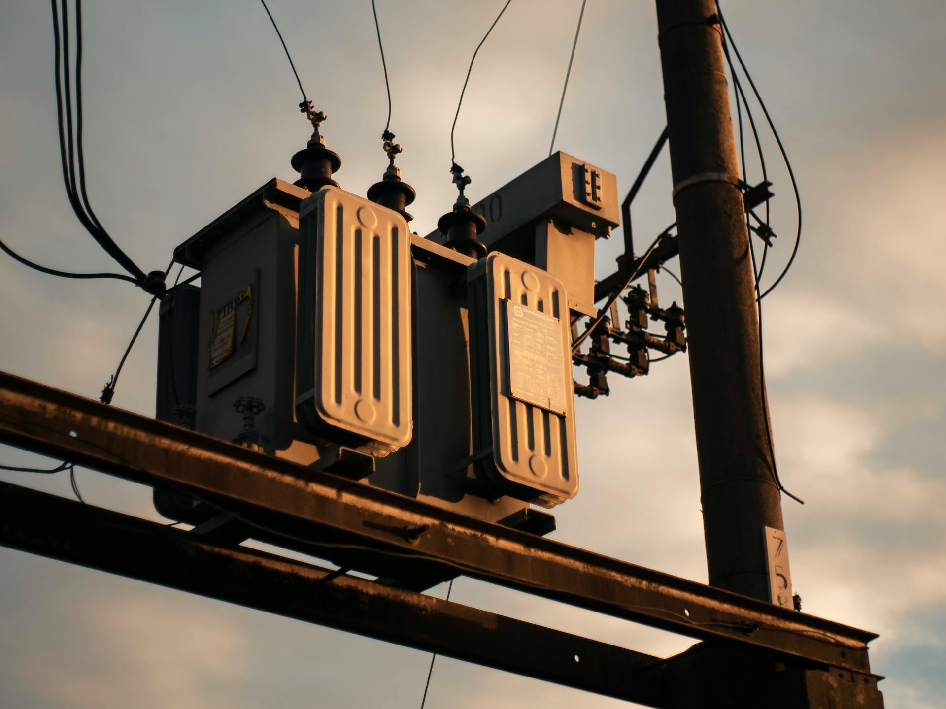 Close-up of an electrical transformer on a utility pole against a sunset sky.