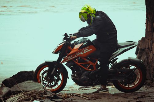 Free A man in a helmet sits on an orange motorcycle by the water. Stock Photo