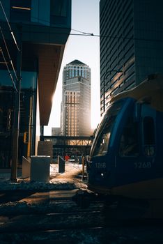 A tram passes through a modern cityscape with tall buildings at sunset.