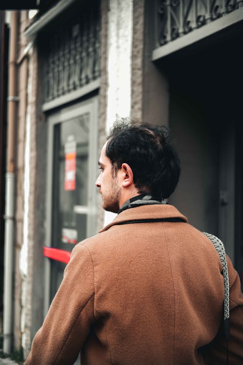Free A Man in Brown Coat Standing Near Building Stock Photo