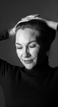 Artistic black and white portrait of a smiling woman with eyes closed and hands on head, wearing a turtleneck.