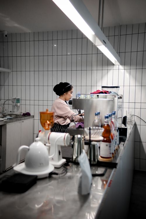 Free A woman working in a modern café, focusing on coffee preparation with bottles and equipment around. Stock Photo