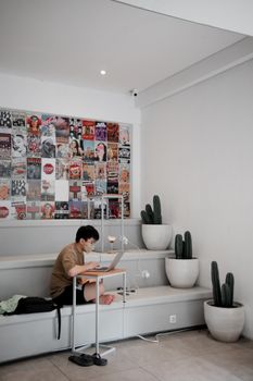 Adult male working on laptop in a modern indoor space, reflecting pandemic lifestyle with face mask and social distancing.