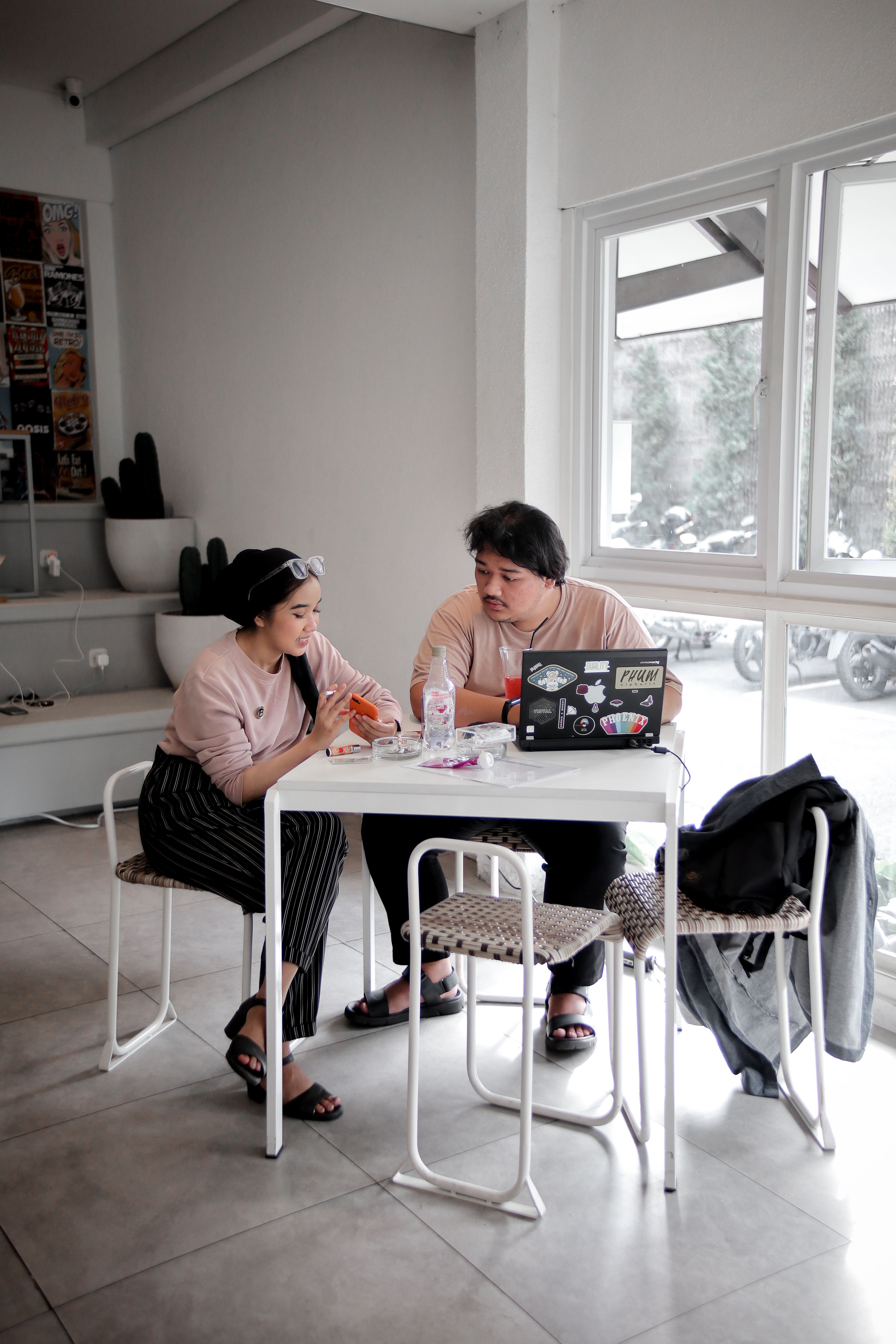 Two adults having a conversation over a laptop in a cozy modern cafe environment.