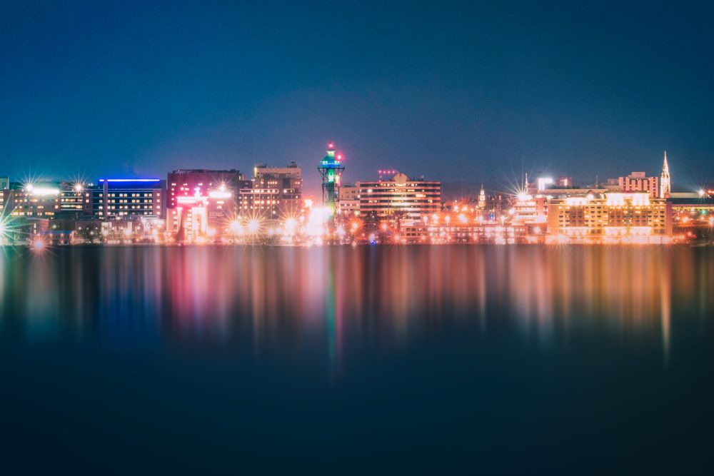 A vibrant city skyline at twilight with reflections on calm water, showcasing modern architecture.