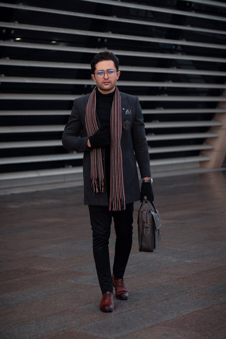 A Man In Black Pants Walking On The Street While Carrying His Bag