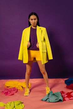 Woman in colorful attire posing against vibrant purple background for fashion shoot.