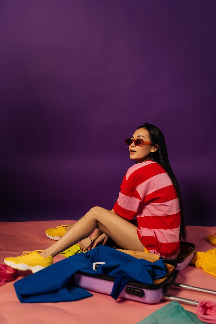 Woman Sitting In Violet Suitcase Full Of Colourful Clothing