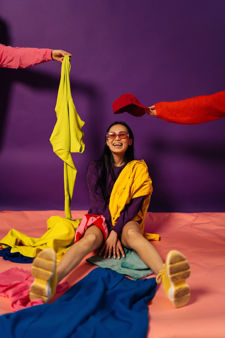 Hands Handing Clothing Articles To Woman Sitting On Floor Laughing